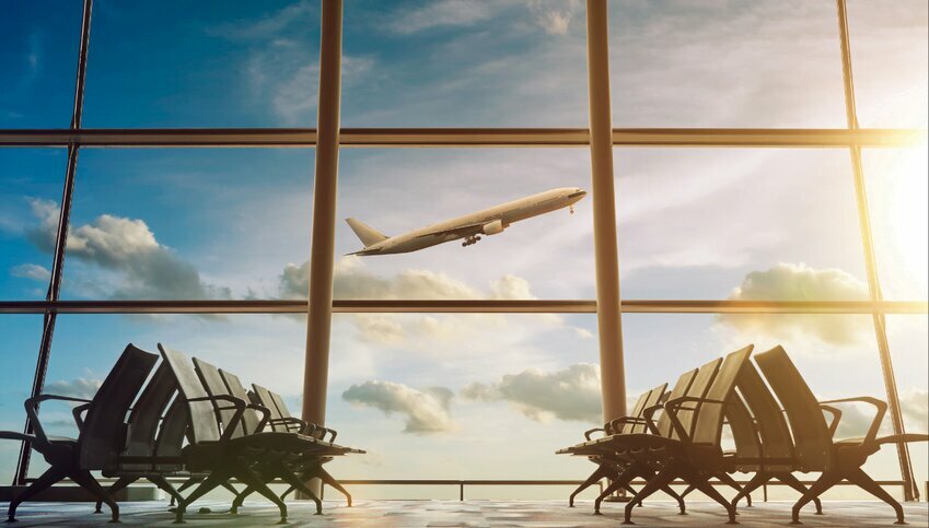 Windows of an airport look out on the horizon of blue skies as an airplane takes off.