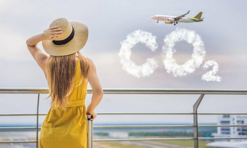 A woman in a yellow dress watching a plane go by with the word "CO2" written in cloud letters, representing emissions.