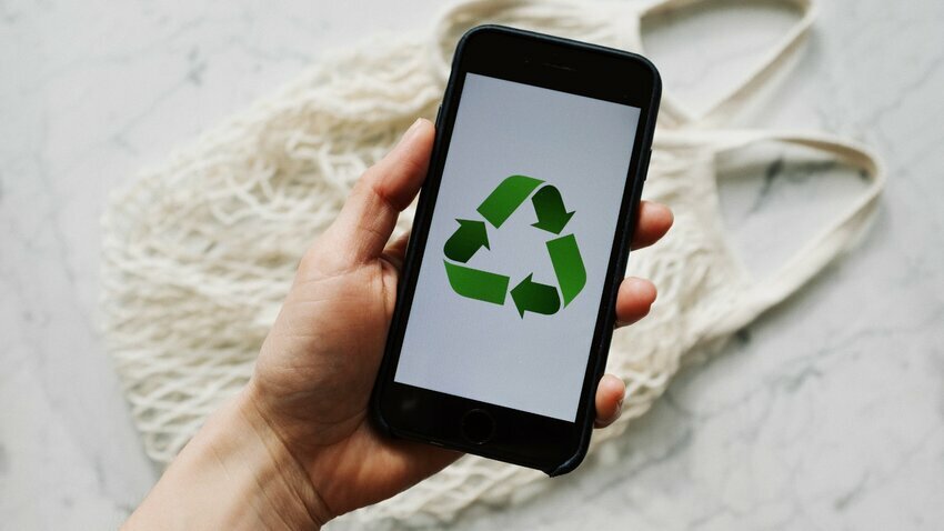 a hand holds a smart phone that has an image of the green recycling triangle