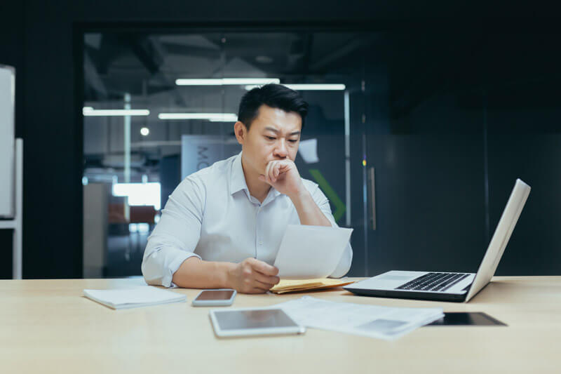 Man sitting in front of a laptop and examining paperwork